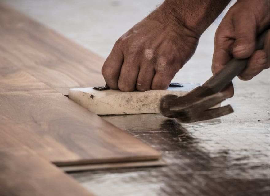Hands smoothing wood with a tool during woodworking.